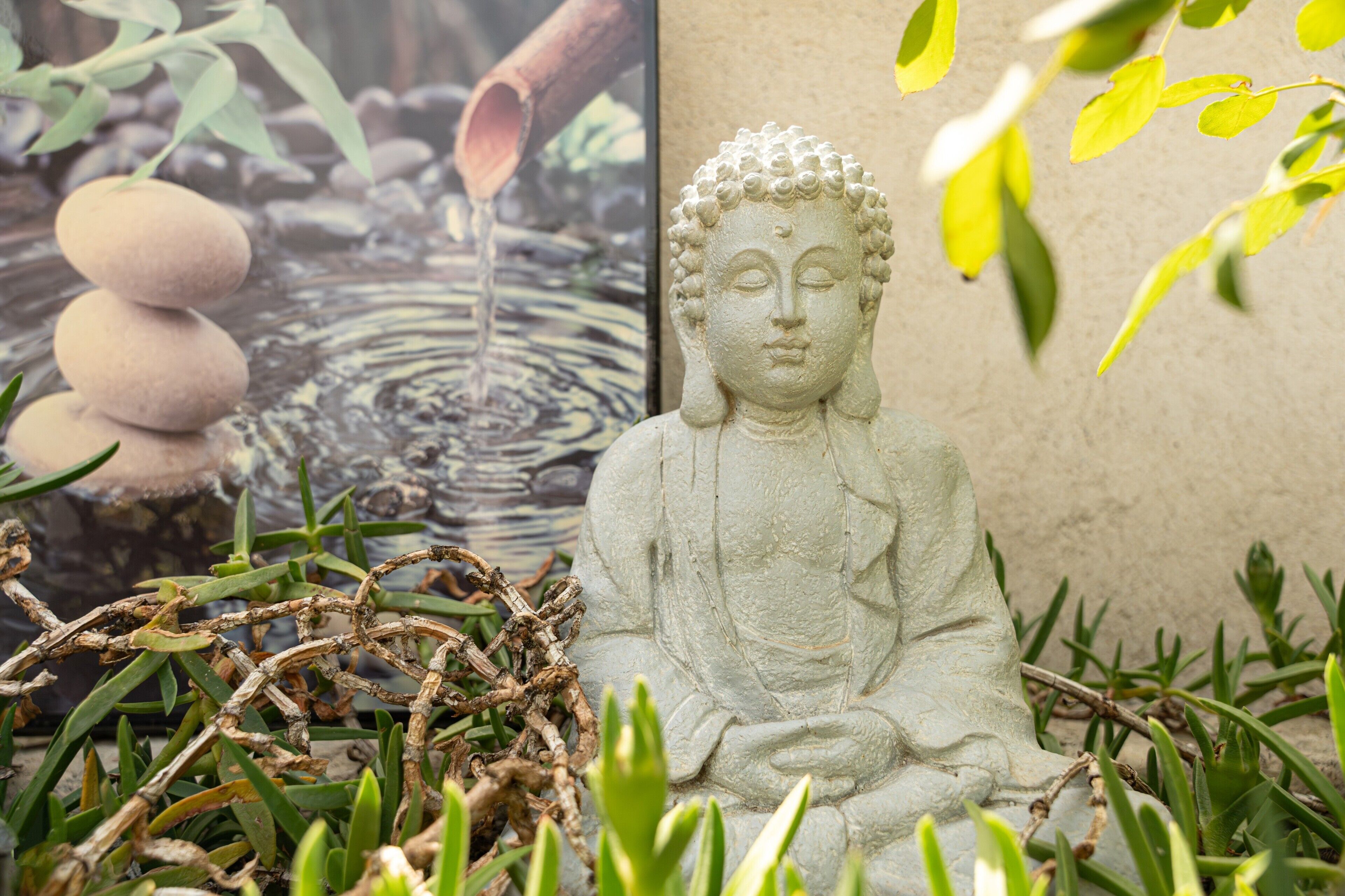 A stone Buddha statue in a garden setting with a water feature and rocks.