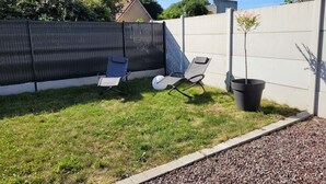A backyard with a lawn, two lounge chairs, a potted plant, and a low wall. - L'Oxybulles and spa (Friville-Escarbotin)