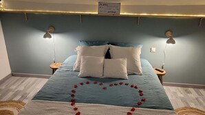 A bedroom with a bed, two bedside lamps, a sign on the wall, and a heart-shaped arrangement of rose petals on the bed. - L'Oxybulles and spa (Friville-Escarbotin)