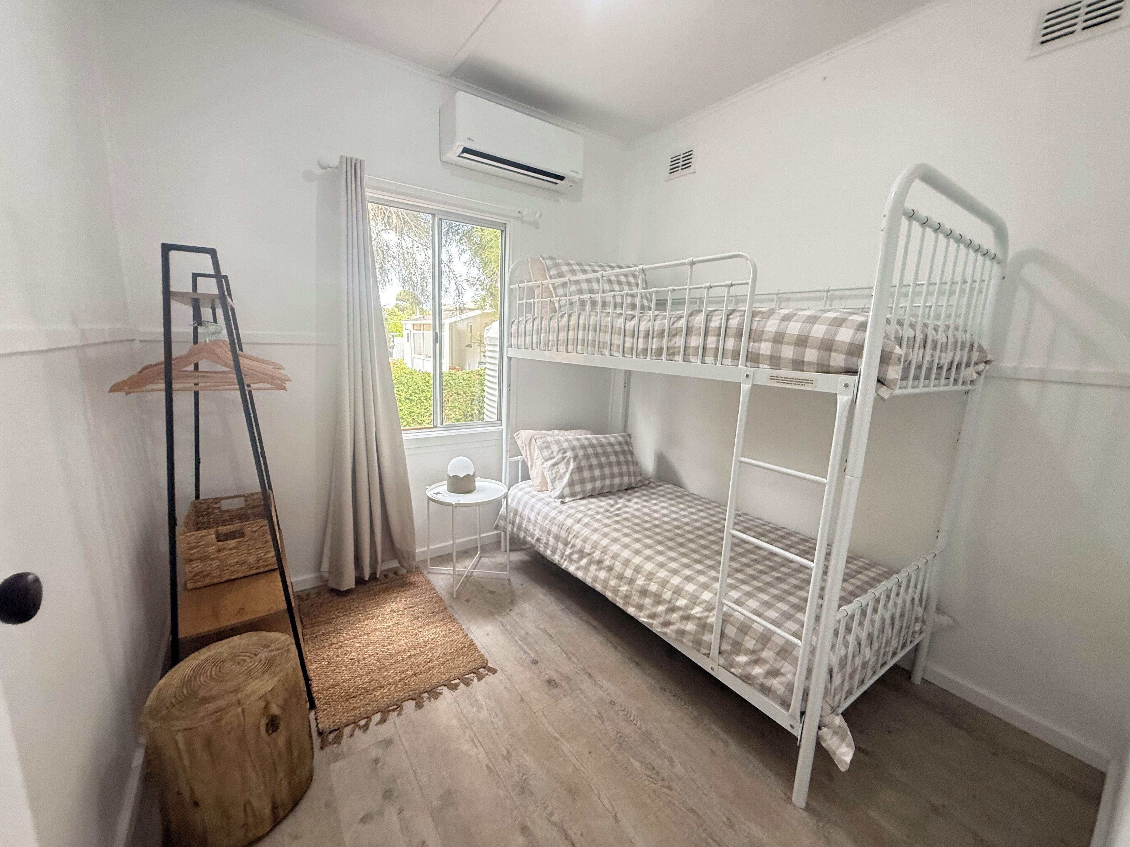 Une chambre avec un lit superposé, une fenêtre, une petite table, un porte-vêtements et un tapis tissé.