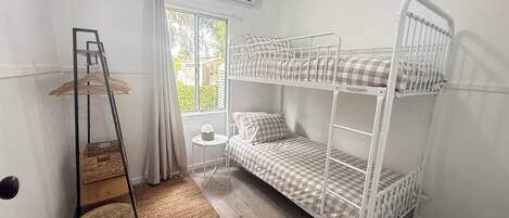 Une chambre avec un lit superposé, une fenêtre, une petite table, un porte-vêtements et un tapis tissé.