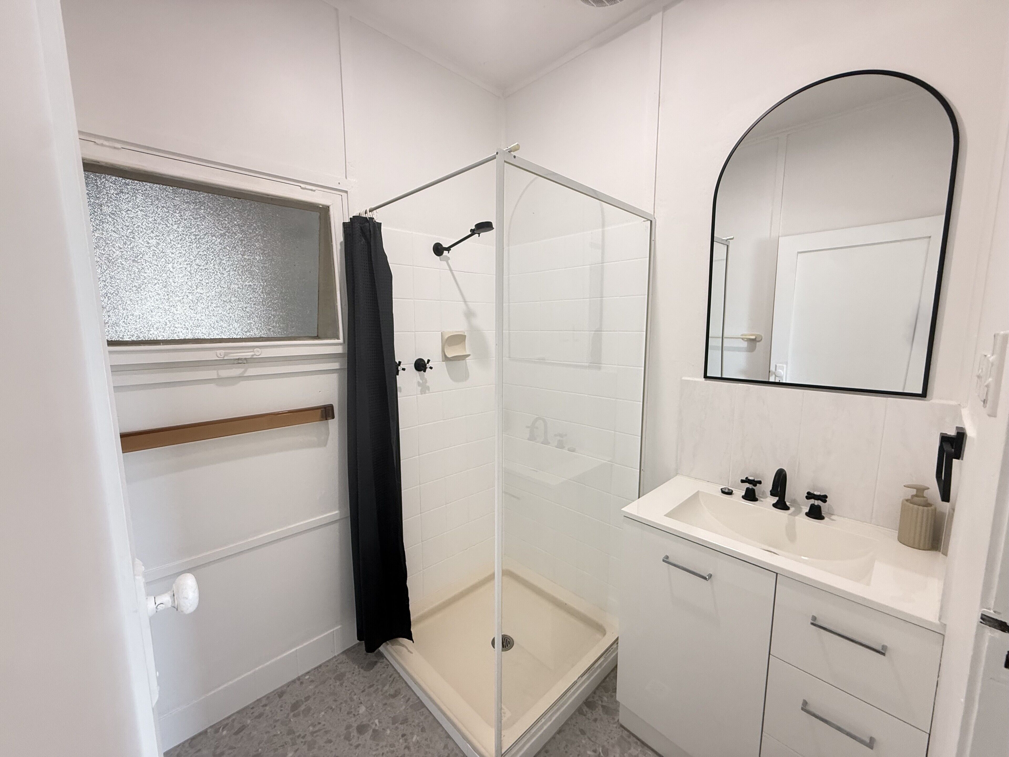 Een badkamer met douche, wastafel en spiegel.
