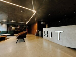 A modern reception area with a minimalist design, featuring a reception desk with the word 'HIT' on it, a seating area with green upholstered chairs, and a clean, tiled floor. - 50m from Cabo Branco beach • High-end apartment (João Pessoa)