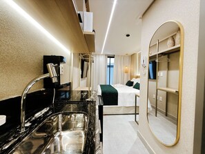 Habitación de hotel con cama, baño con lavamanos y espejo, y mesita de noche.