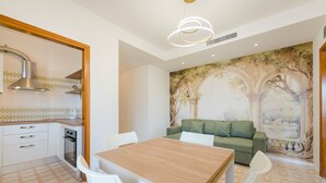 Une cuisine moderne avec des meubles blancs, une table à manger en bois et un canapé vert.