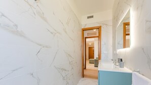 Une salle de bain aux murs recouverts de marbre, un lavabo avec un miroir et une porte donnant sur une autre pièce.