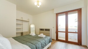 Une chambre à coucher comprenant un lit, une table de chevet, un miroir, une armoire et une porte-fenêtre coulissante donnant sur un balcon.
