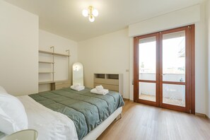 Ein Schlafzimmer mit Bett, Nachttisch, Spiegel, Kleiderschrank und einer Schiebetür zum Balkon.