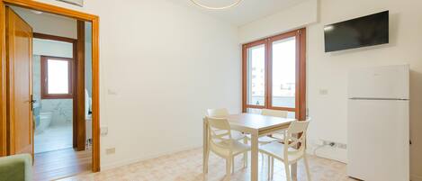 A kitchen with a dining table, chairs, a TV, and a refrigerator.
