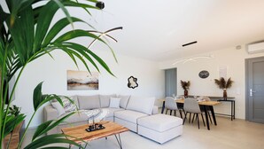 A modern living room with a sectional sofa, a wooden coffee table, and a dining area with a table and chairs. - Etherio Naxos Ouranos Charming 2-bedroom apartment with AC in beautiful Naxos (Cyclades)