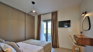 A bedroom with a bed, a desk, a chair, a TV, and a sliding glass door. - Etherio Naxos Ouranos Charming 2-bedroom apartment with AC in beautiful Naxos (Cyclades)