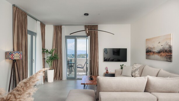 A modern living room with a sofa, a flat-screen TV, a painting, and a balcony with a view. - Etherio Naxos Ouranos Charming 2-bedroom apartment with AC in beautiful Naxos (Cyclades)