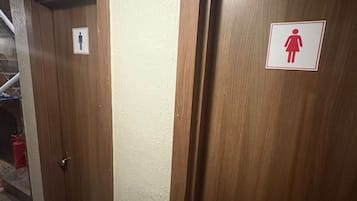 Corredor com duas portas de madeira, uma identificada para homens e outra para mulheres, dando acesso a quartos privativos.