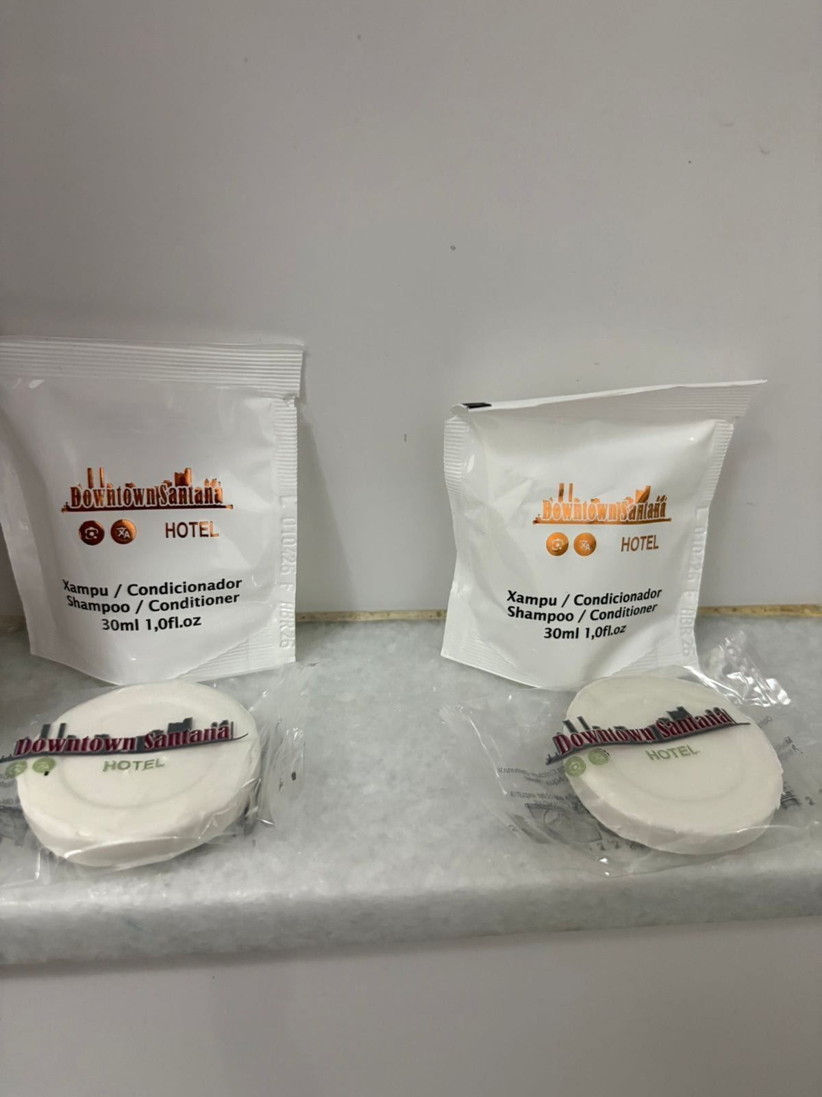 Deux emballages de shampoing et d’après-shampoing provenant de l’hôtel Downtown Santaná, chacun portant le logo de l’hôtel et les informations sur le produit.