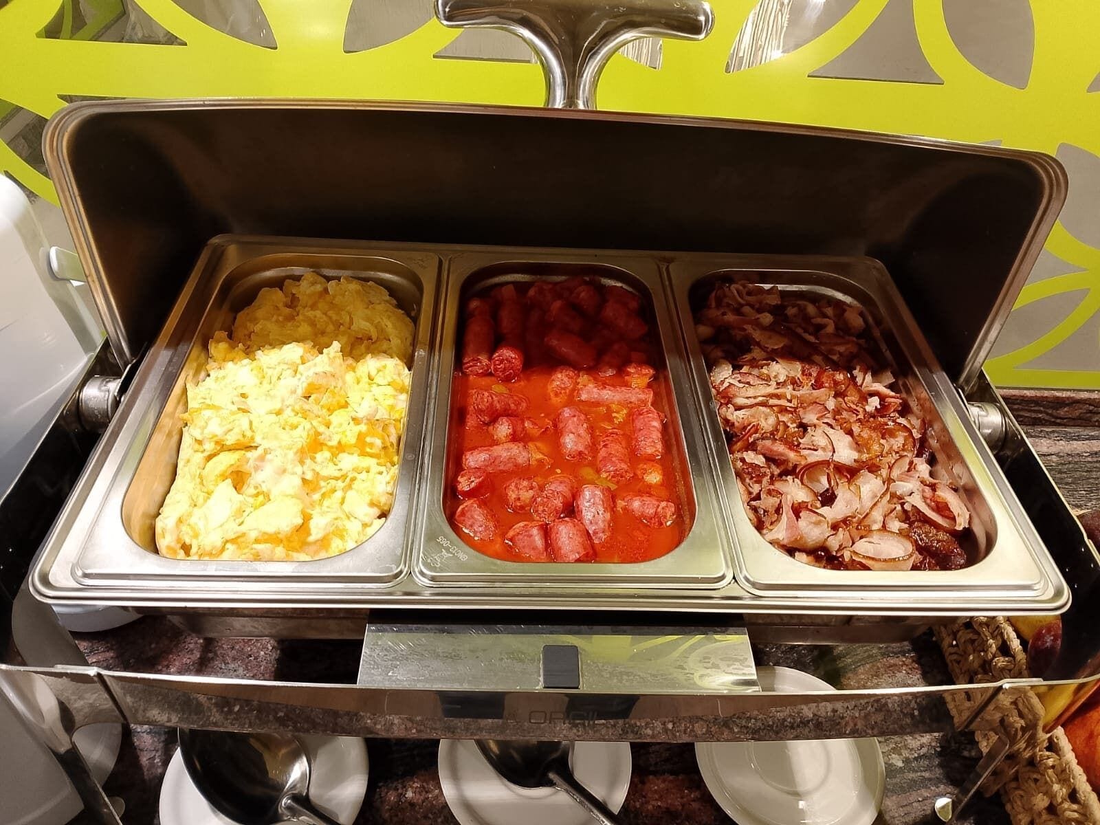 A buffet with scrambled eggs, sausage in tomato sauce, and bacon.