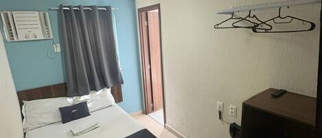 Habitación de hotel con cama, un escritorio pequeño, un calentador, un perchero y una puerta que da a otra habitación.
