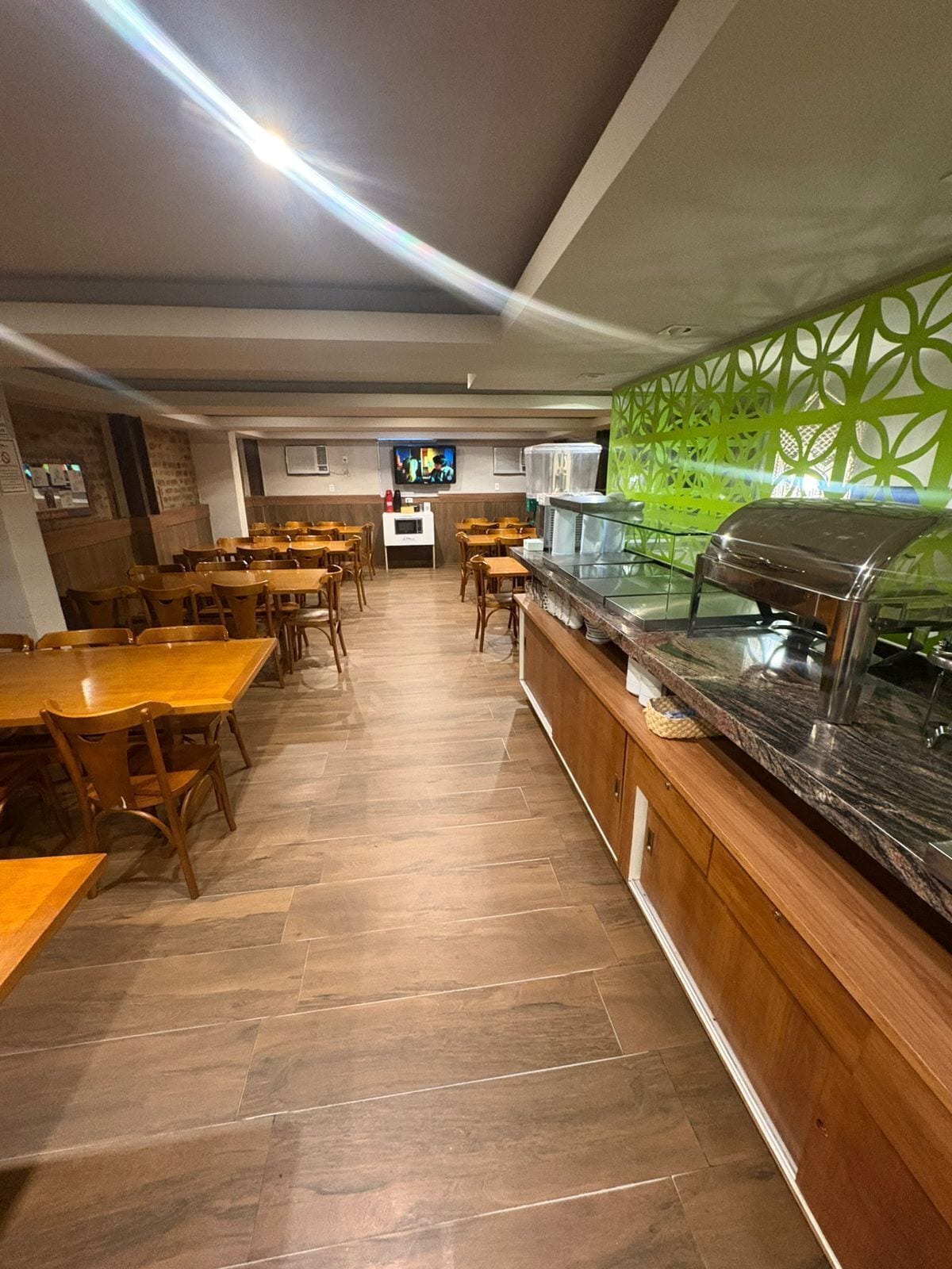 Un restaurant avec des tables et des chaises en bois, un comptoir avec un grill et un écran de télévision en arrière-plan.