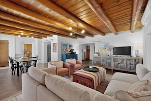 A spacious living area with wooden beams, a dining table, sofas, and a TV. - Old Charm Adobe Home, 3bd/2ba, Grill, Firepit (Albuquerque)