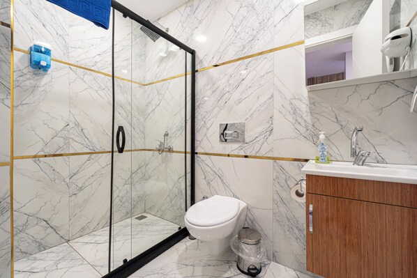 A modern bathroom with a glass-enclosed shower, a white toilet, and a wooden vanity. - Mall Of Palace Hotel (İstanbul)