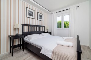 Ein Schlafzimmer mit einem Bett, Nachttischen, einem Fenster mit Vorhängen und Streifenmuster-Tapete.