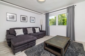 Ein modernes Wohnzimmer mit einer Eckcouch, einem Couchtisch und einem großen Fenster mit Vorhängen.