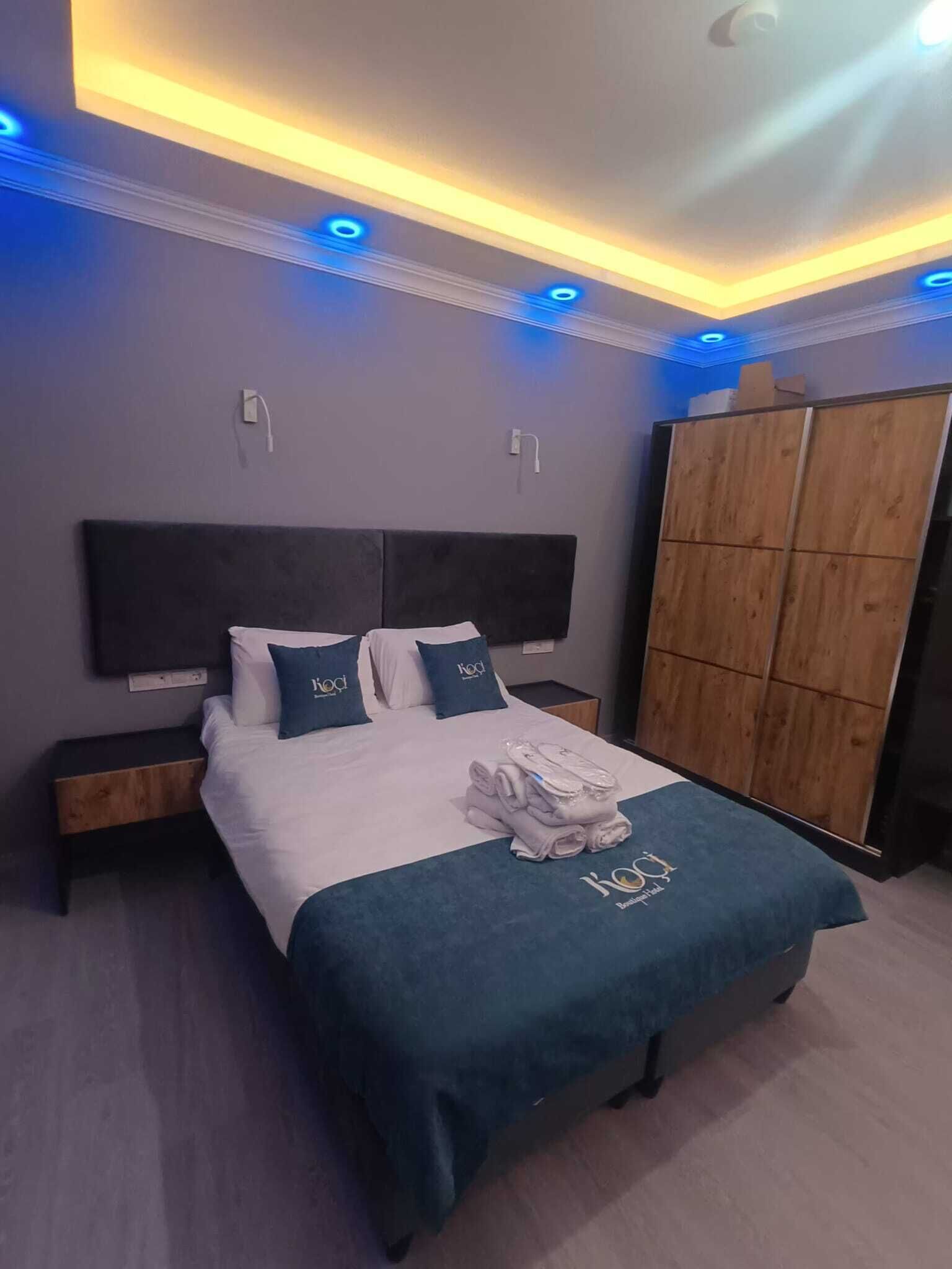 Ein ordentlich bezogenes Bett mit blauem Kopfteil, einem Holzschrank und einer Decke mit blauen LED-Leuchten.