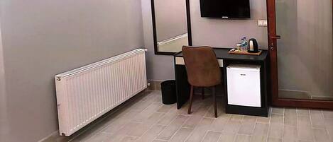 A room with a desk, chair, a small refrigerator, a television mounted on the wall, and a door with a frosted glass panel.