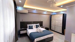 A modern bedroom with a bed, bedside tables, a ceiling fan, and built-in storage cabinets. - Koçi Hotel (Pazar)