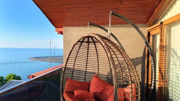 A wicker swing chair with cushions on a balcony overlooking the sea. - Koçi Hotel (Pazar)