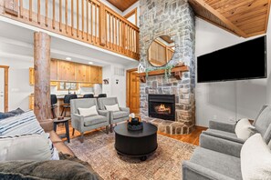 A spacious living area with a stone fireplace, a flat-screen TV, and a high ceiling with wooden beams. - NEW! King Suites Private Baths, Near Silver Dollar (Branson West)