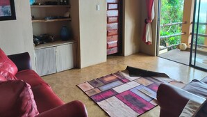 Een woonkamer met een rode bank, een kamerbreed tapijt en uitzicht op de omgeving door een schuifdeur.