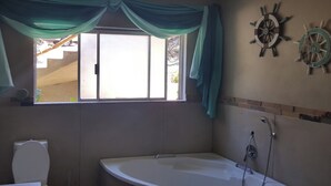 Een badkamer met een bad, een raam met gordijnen, en twee decoraties van scheepswielen.
