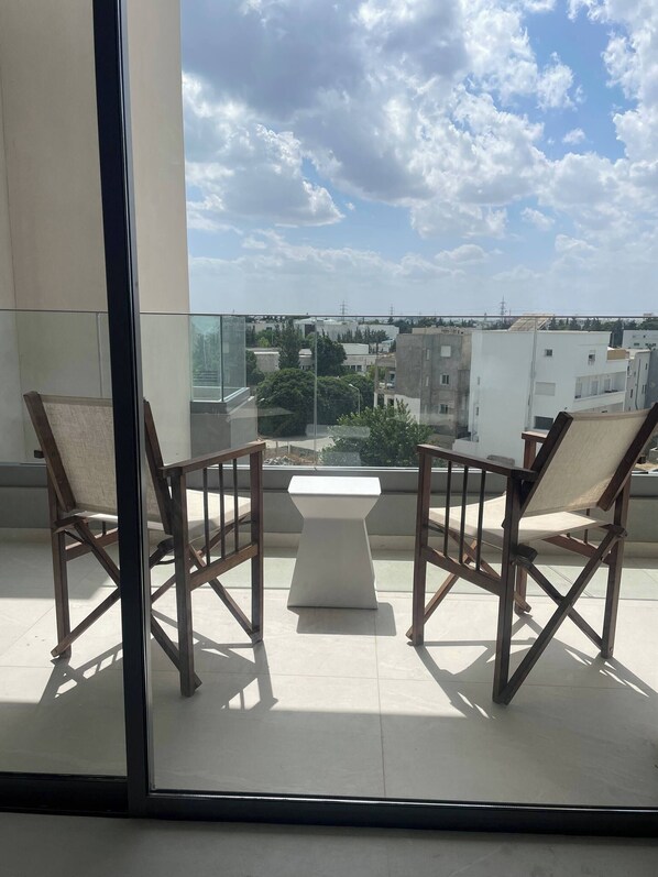 A balcony with two wooden chairs and a small table, overlooking a cityscape with buildings and trees. - Zeyna Apartment La Marsa (La Marsa)