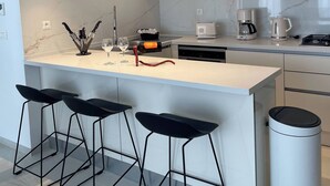 A modern kitchen with white cabinets, a marble countertop, a central island with bar stools, and pendant lighting. - Zeyna Apartment La Marsa (La Marsa)