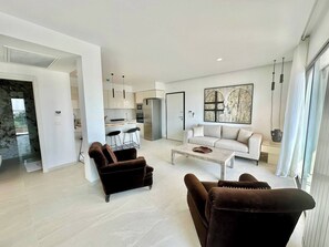 Ein modernes Wohnzimmer mit einer Couch, zwei Sesseln, einem Couchtisch und einer Küche im Hintergrund.
