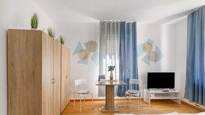 Une chambre à coucher comprenant un lit, une télévision, un bureau, deux chaises, une armoire et des éléments décoratifs muraux.
