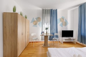 Un dormitorio con cama, televisión, escritorio, dos sillas, armario y decoración en la pared.