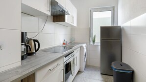 Une cuisine compacte équipée d’un réfrigérateur en acier inoxydable, d’un four encastré, d’une machine à café et d’un lave-linge.