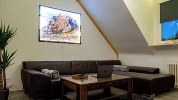 Ein Loft-Wohnzimmer mit schrägem Dach, einem braunen Ledersofa, einem Holztisch mit einem Laptop und einem großen gerahmten Bild an der Wand.
