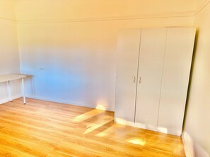 A room with a white wardrobe, a small white table, and wooden flooring.