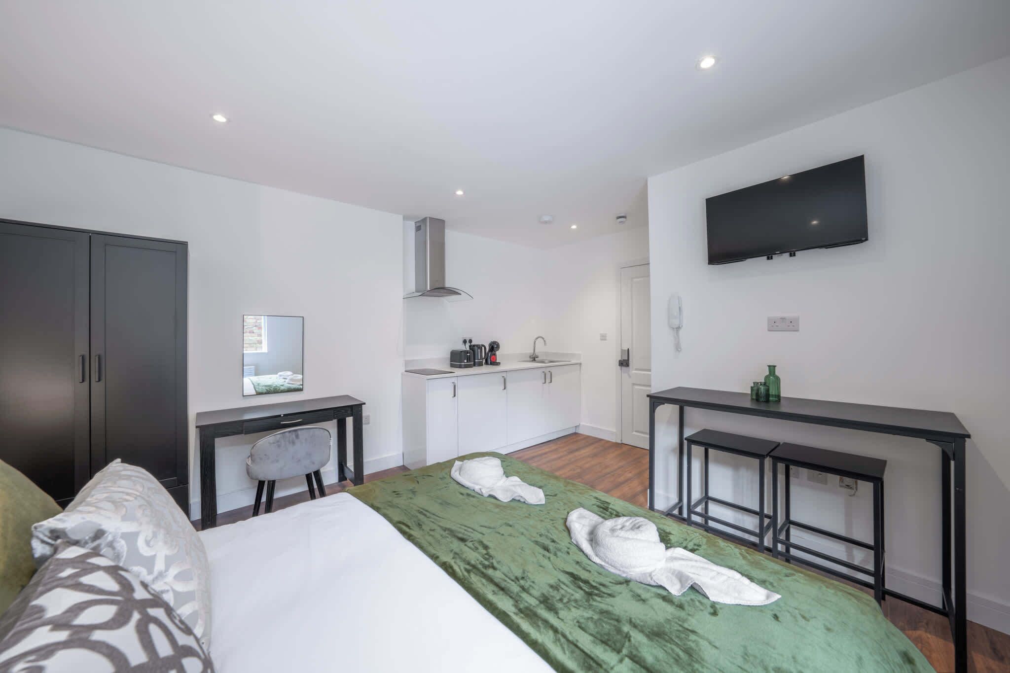 Een moderne hotelkamer met een bed, bureau, kitchenette en televisie.
