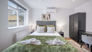 Une chambre d’hôtel moderne, dotée d’un grand lit, d’un bureau, d’une armoire et d’une fenêtre donnant sur des immeubles.