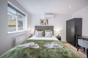 A modern hotel room with a large bed, a desk, a wardrobe, and a window with a view of buildings. - Modern Studio in Knightsbridge (London)
