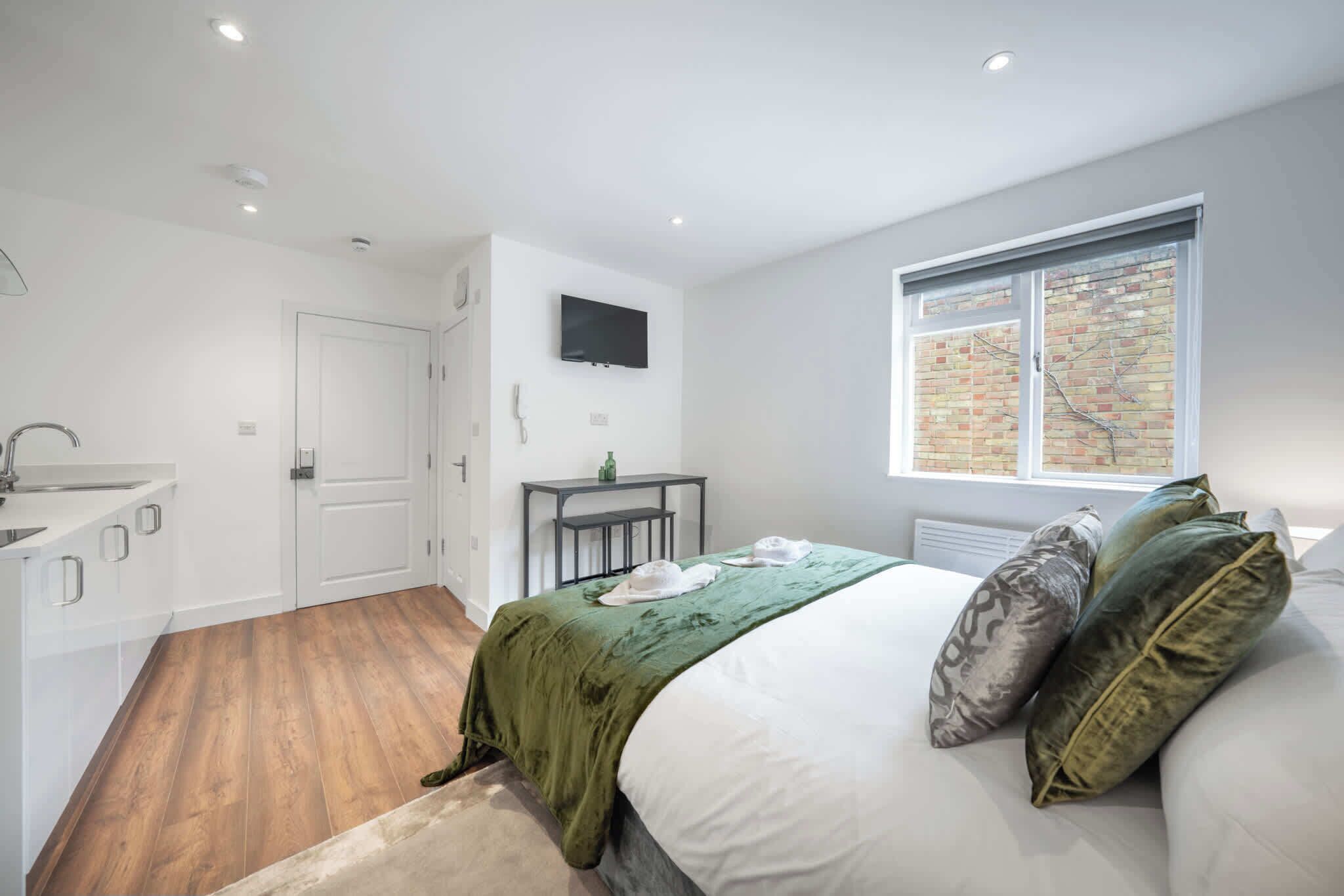 A bedroom with a bed, pillows, a TV, a window, a desk, and a bathroom.