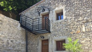 A stone building with a wooden door, a balcony with a metal railing, and outdoor seating. - Loft San Francisco (Baix)