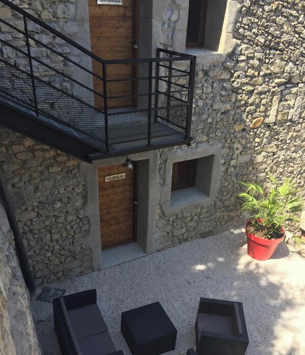 Edificio de piedra con puerta de madera que dice 'LOS ANGELES', un balcón con barandilla de metal y asientos exteriores con macetas.