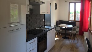 A compact kitchen with modern appliances, a dining area with a round table and chairs, and a large window with curtains. - Loft San Francisco (Baix)
