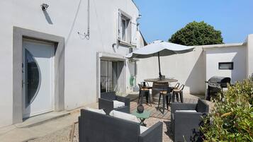 A patio with outdoor furniture, a grill, and a white building with a door and windows.