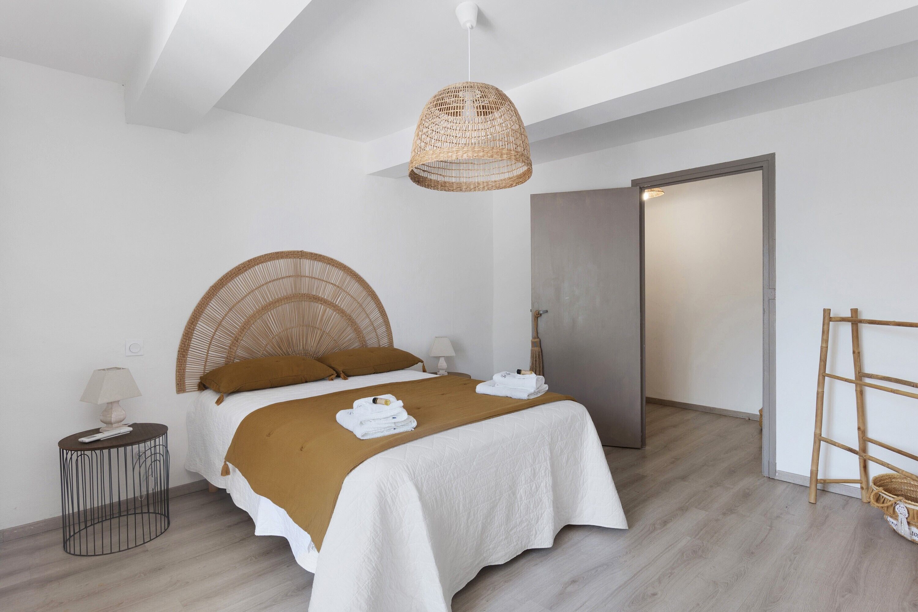 A modern bedroom with a bed, bedside tables, a hanging light fixture, and a wooden ladder.