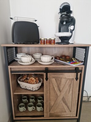 Une petite cuisine équipée d’une machine à café, de pots, de tasses et d’un plateau de collations.